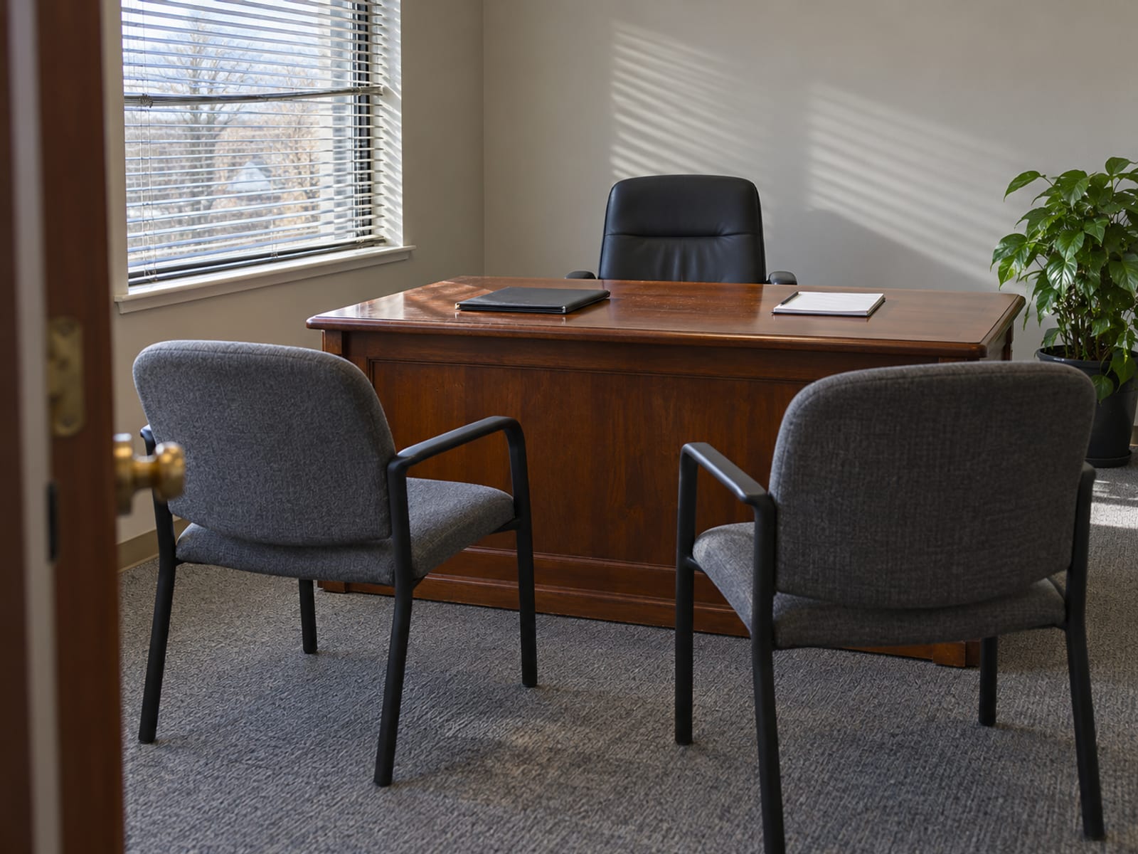 Two chairs facing a desk with a folder and a notepad in a bright small office, no one seated