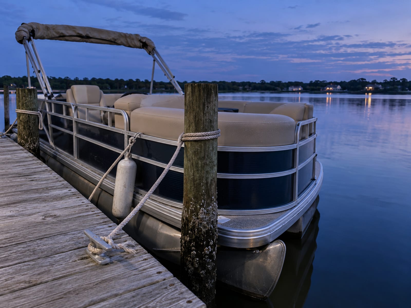 A pontoon boat tied to a wooden dock on a calm bay at dusk