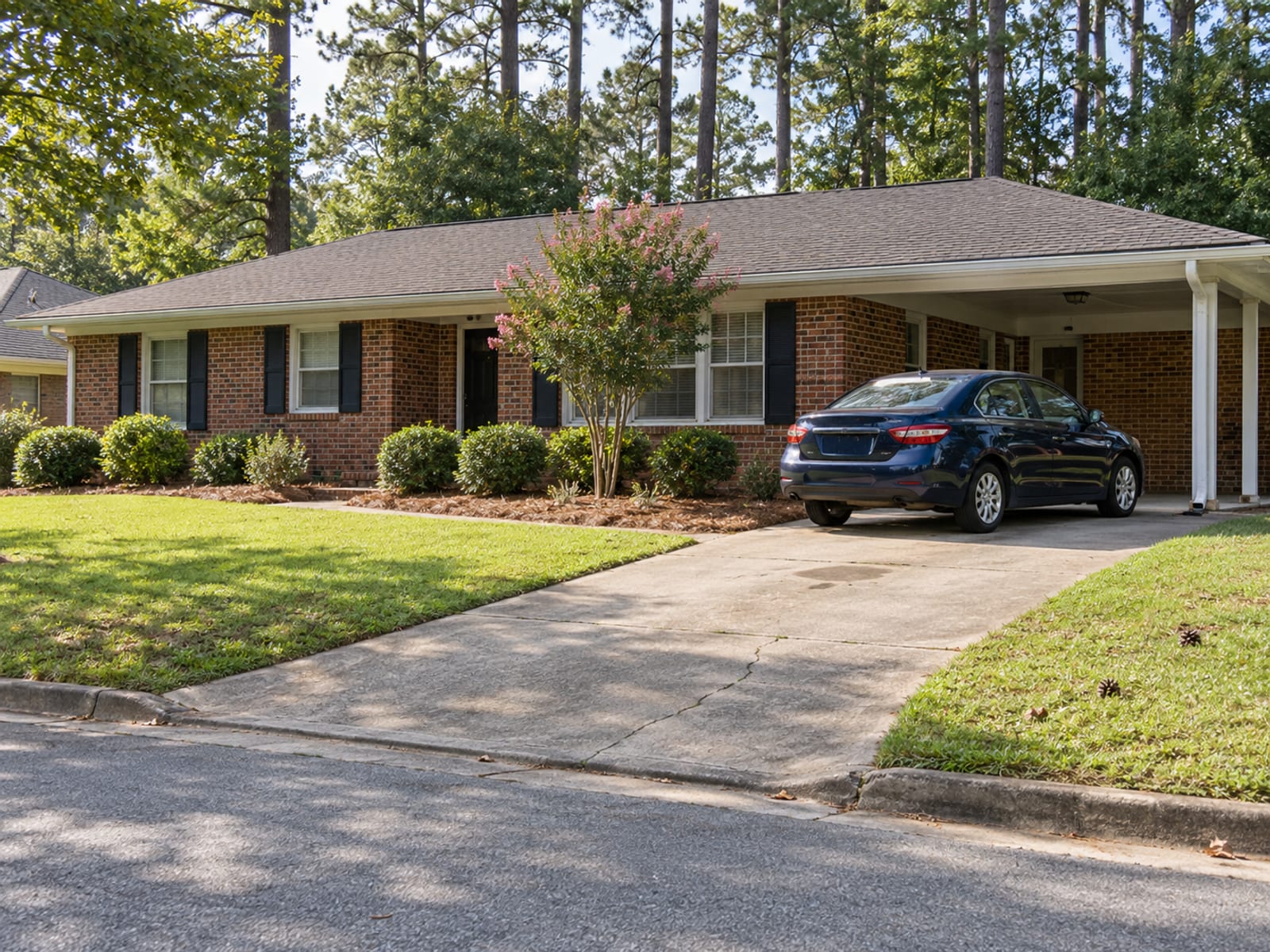 A sedan parked in the driveway of a brick ranch house on a sunny afternoon