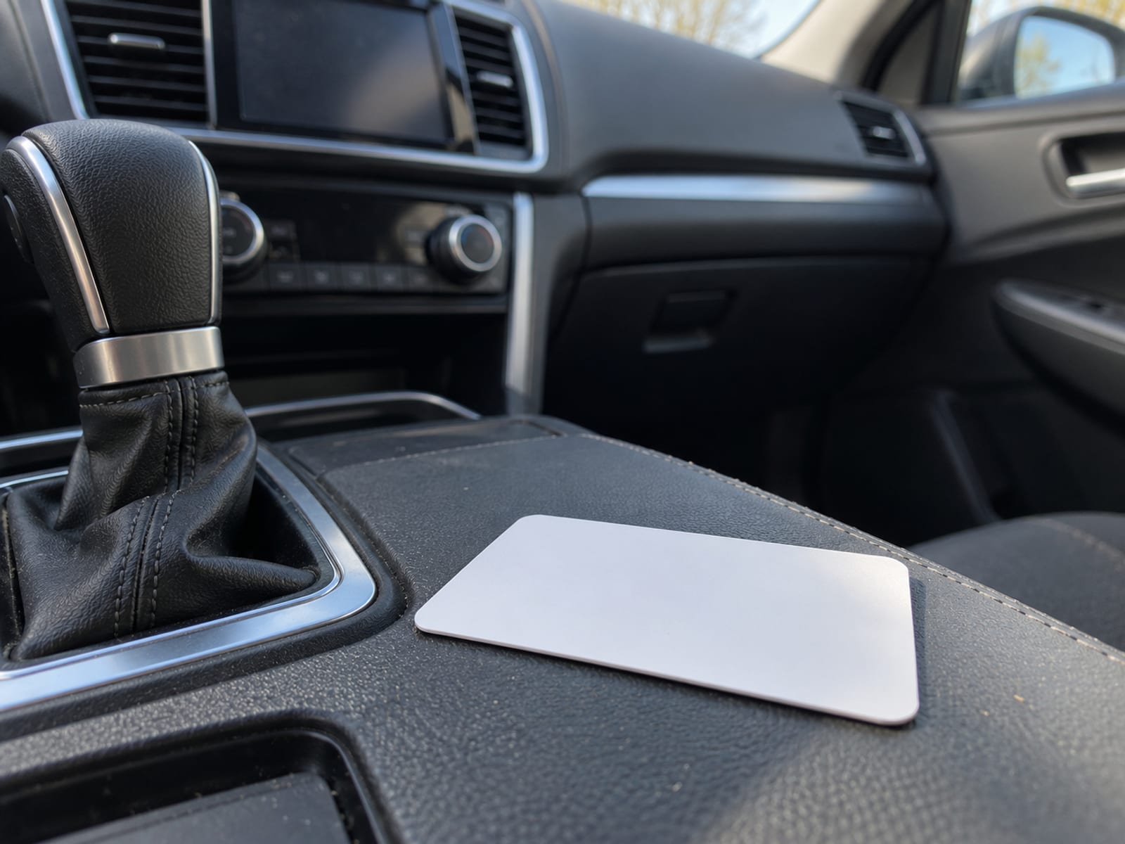 A blank, unprinted insurance-style card resting on a car's center console beside the dashboard