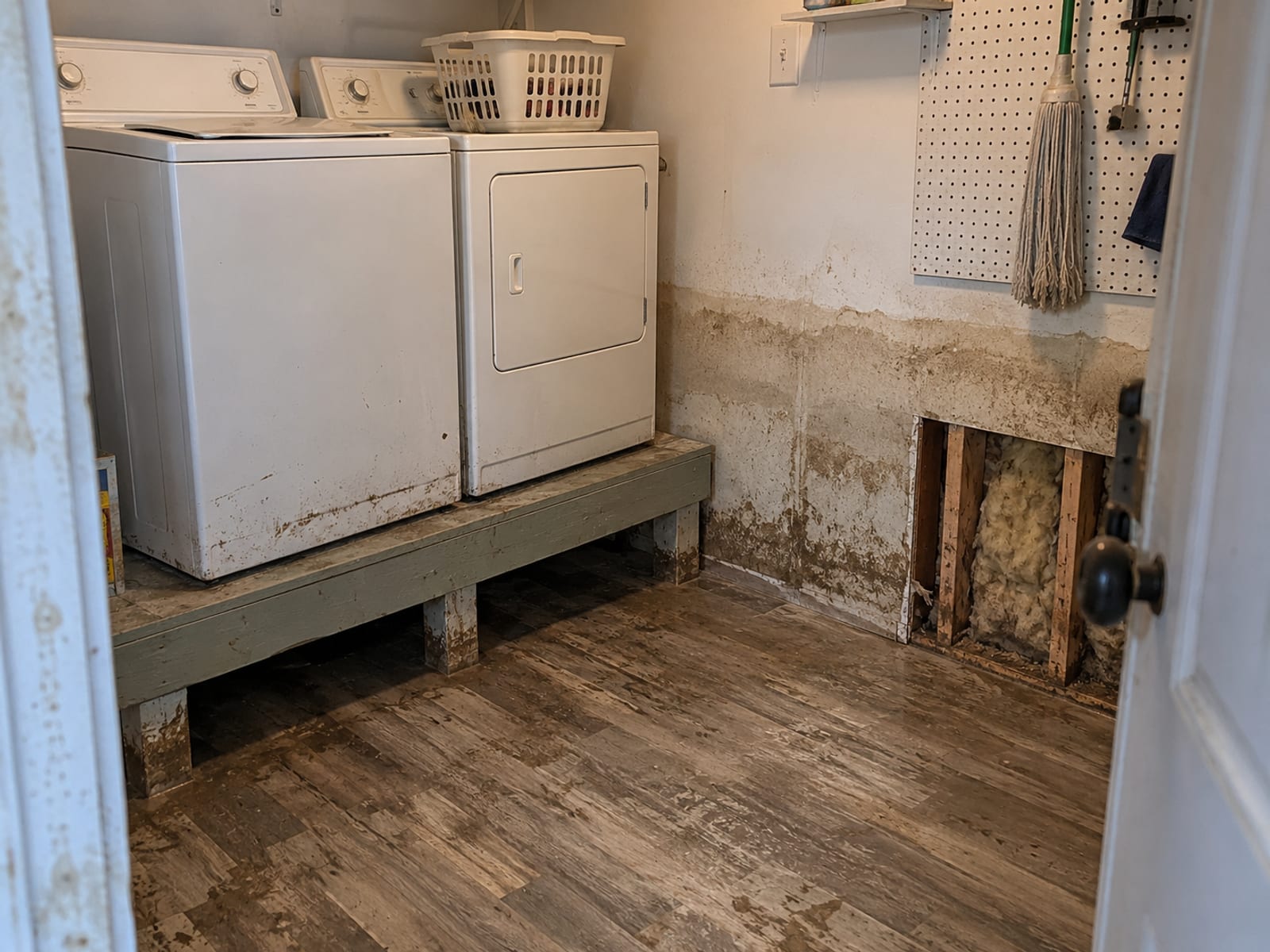 Water-stained drywall and a raised washer and dryer in a home utility room after a flood