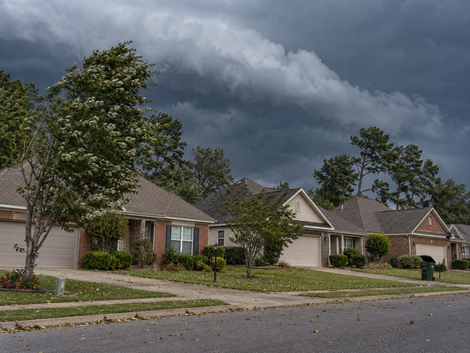 Storm clouds building over a row of suburban homes with shingle roofs