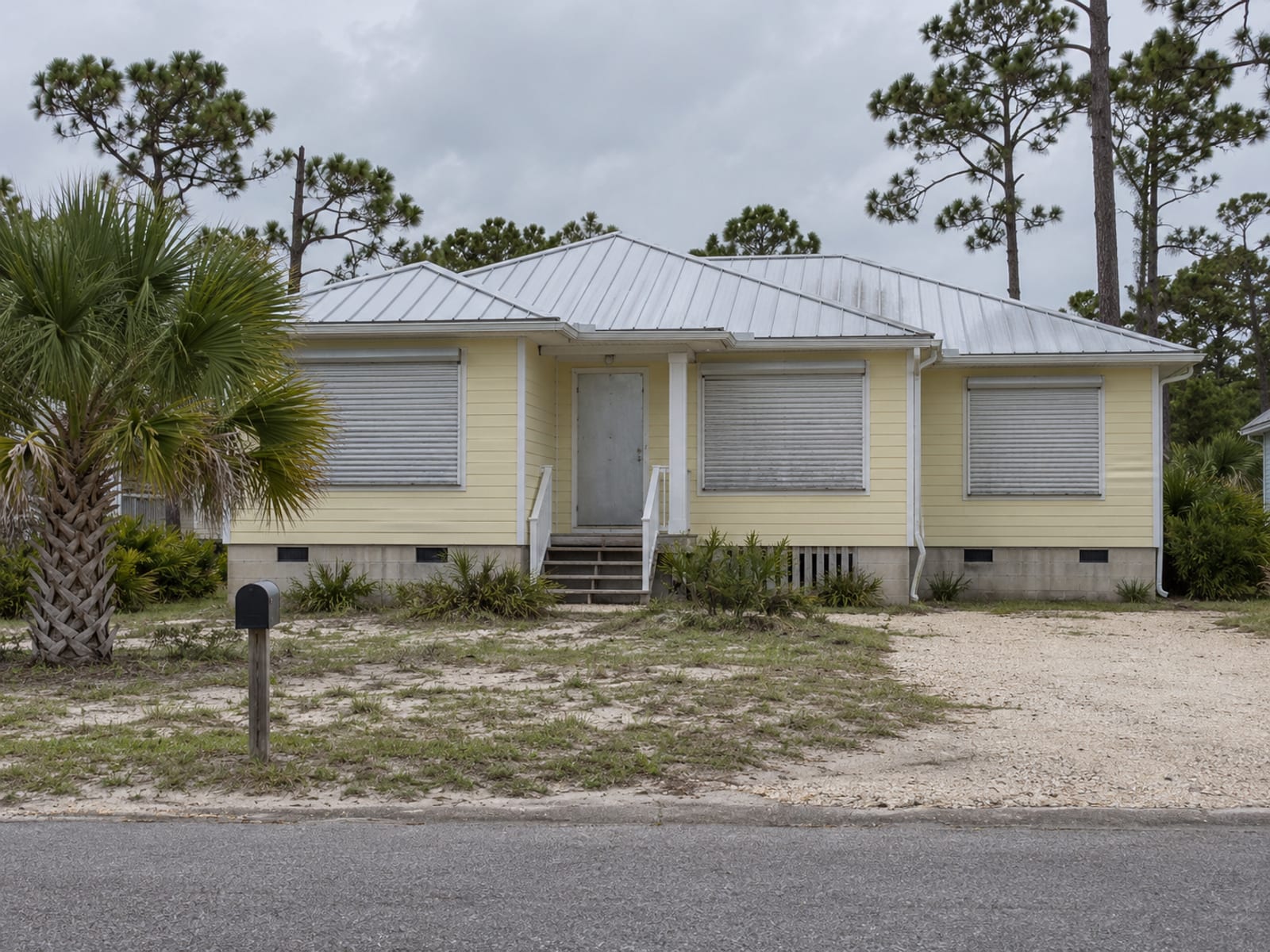 A single-story coastal home with closed storm shutters under a gray sky