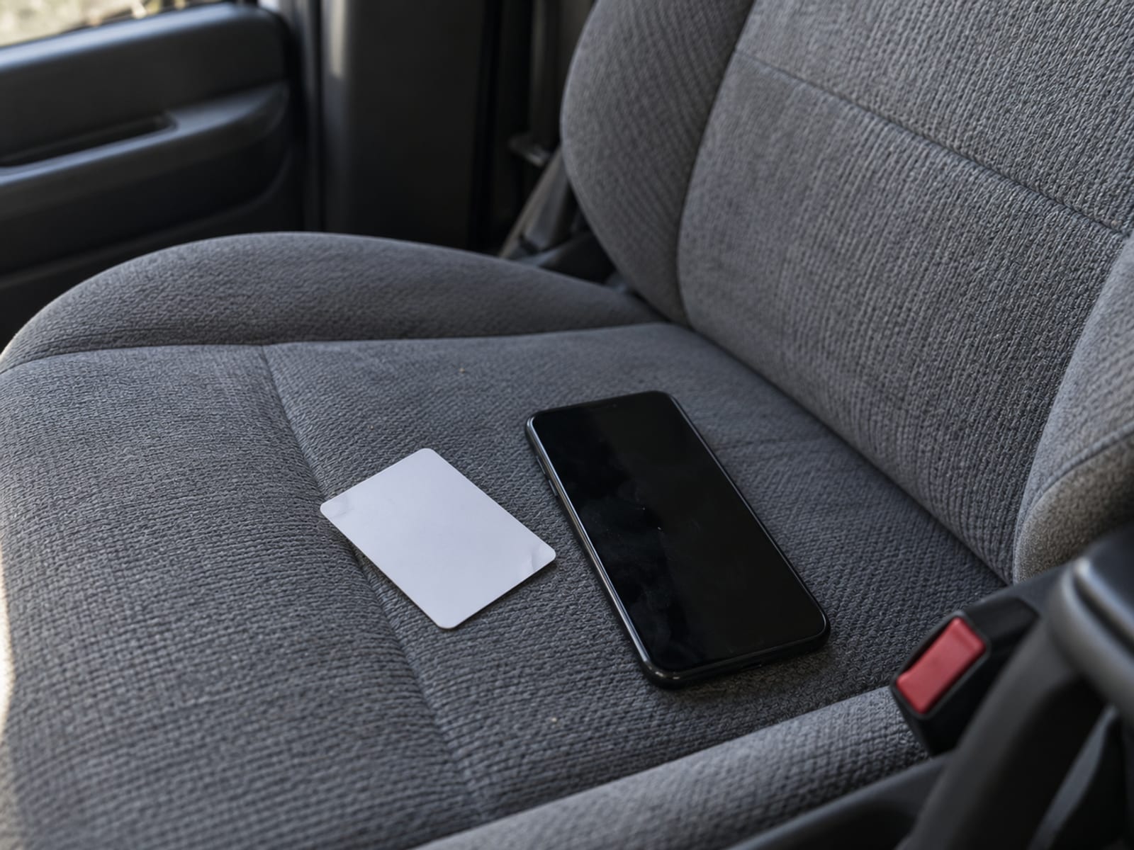 A blank, unprinted insurance-style card lying next to a smartphone with a dark screen on a car seat