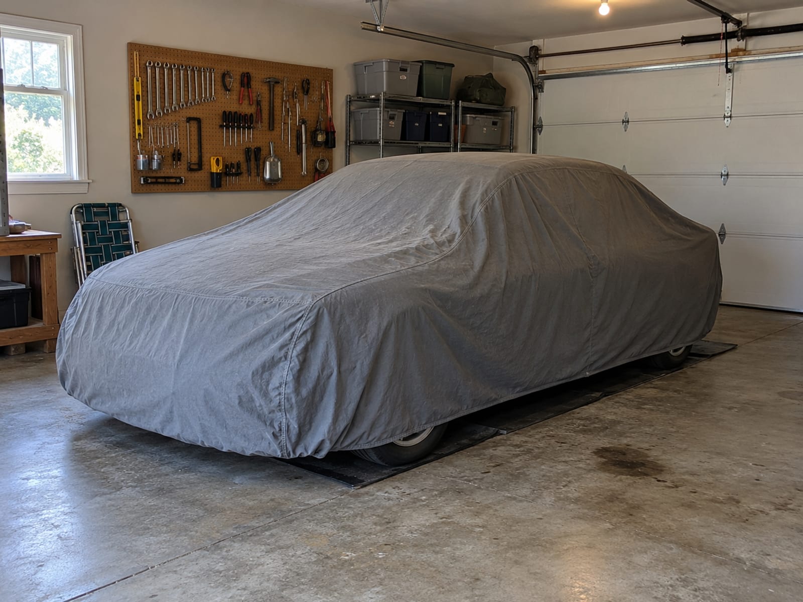 An older car parked under a fitted cloth cover in a home garage