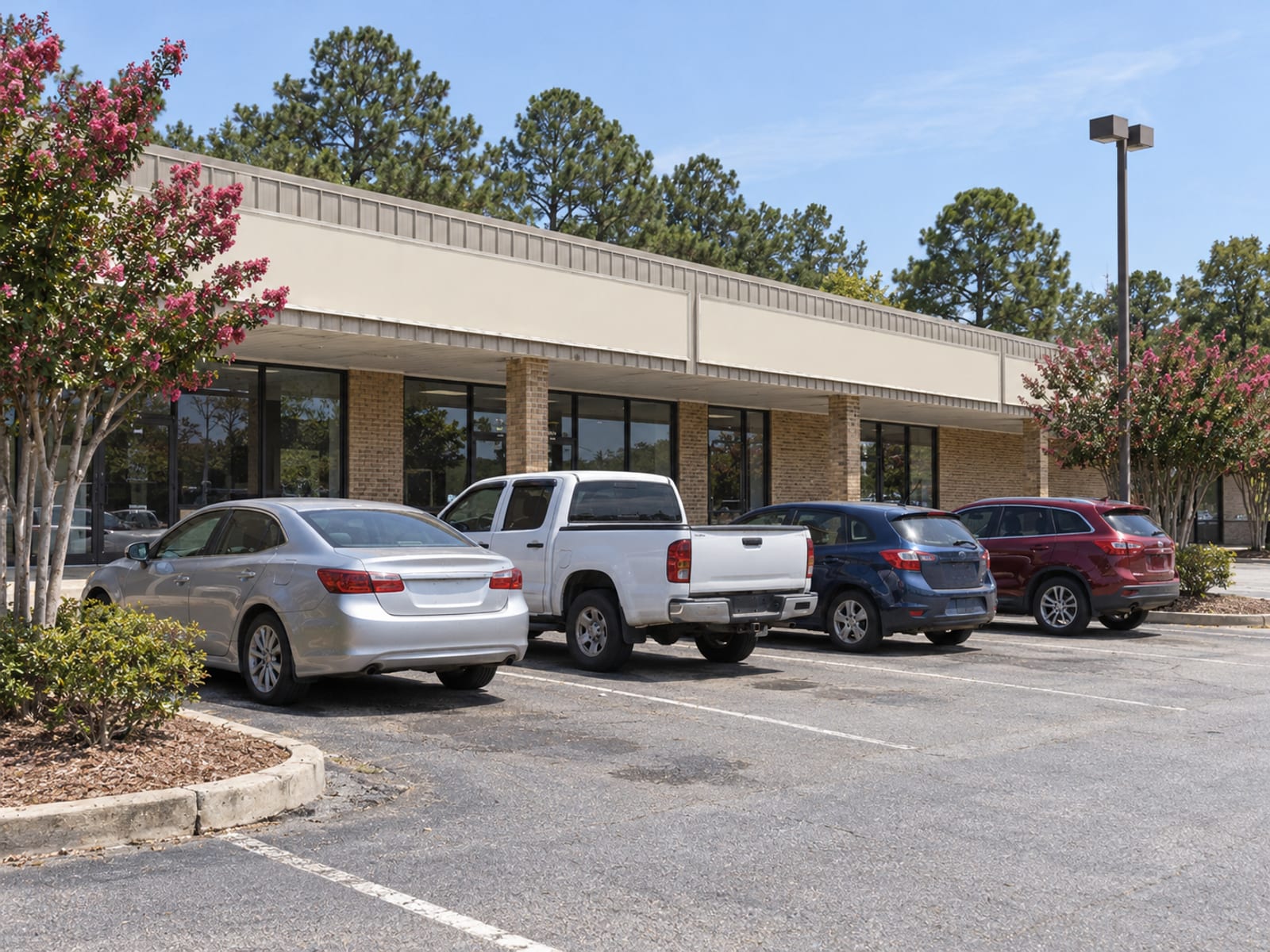 Una fila de autos estacionados afuera de un centro comercial pequeño de un pueblo de Alabama en un día despejado
