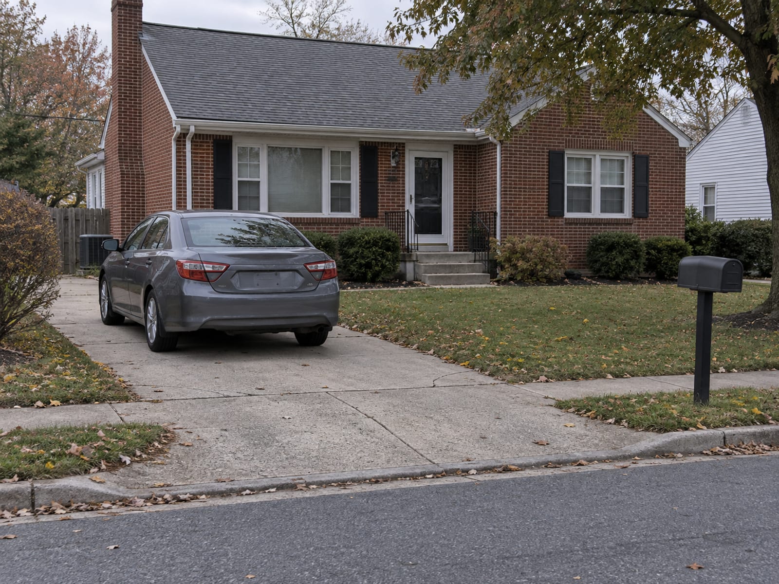 A family car parked in the driveway of a brick Delaware home beside a small front lawn