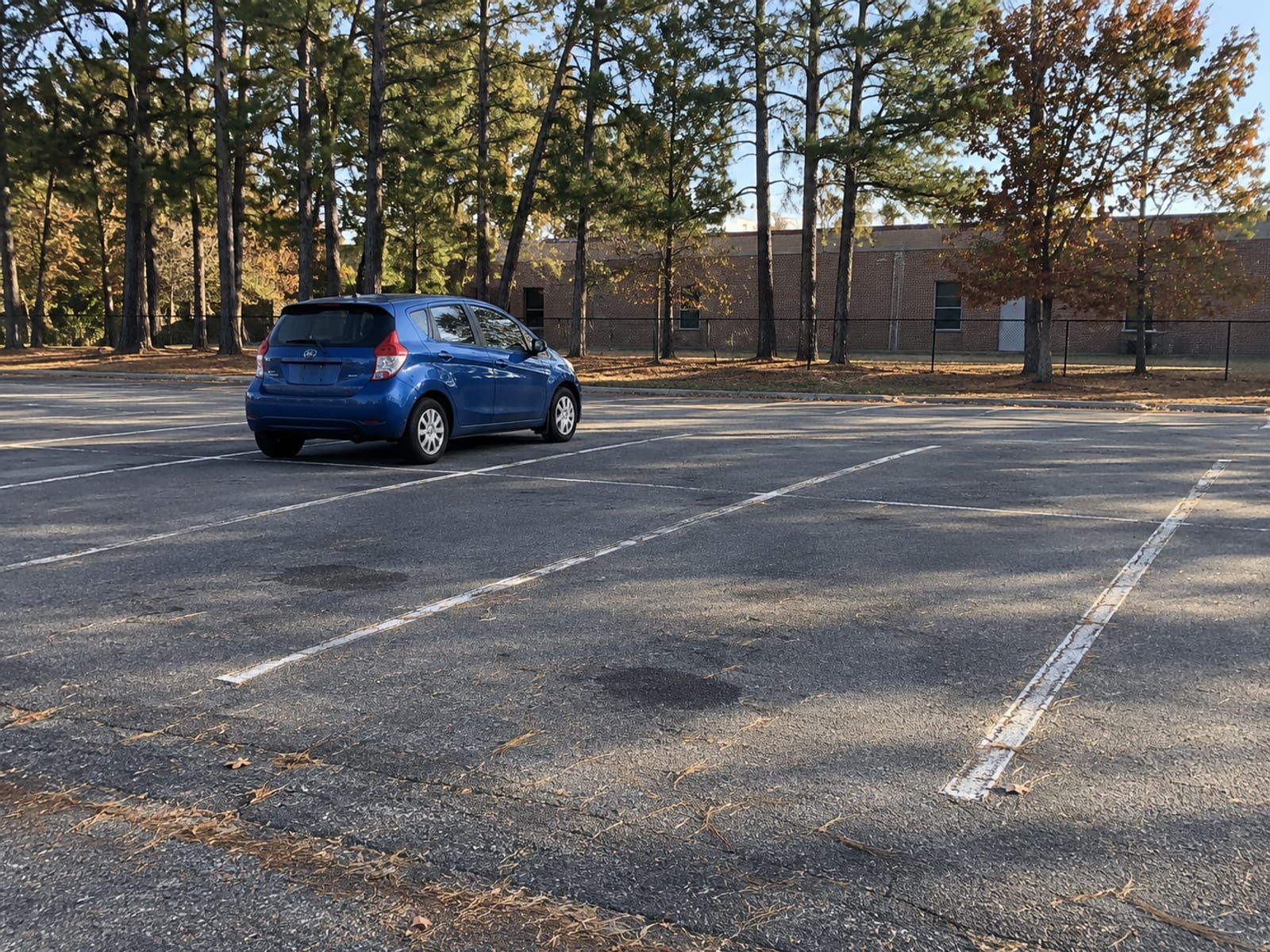 A compact car parked alone in an empty school parking lot in late afternoon