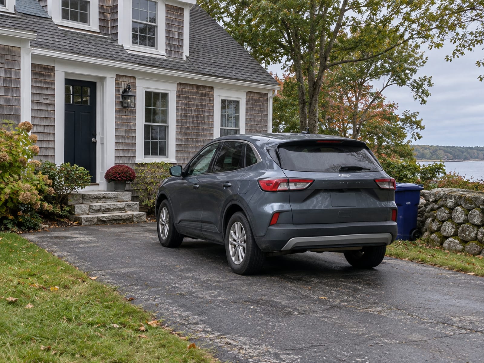 A family car parked in the driveway of a shingled Maine home with a small attached garage