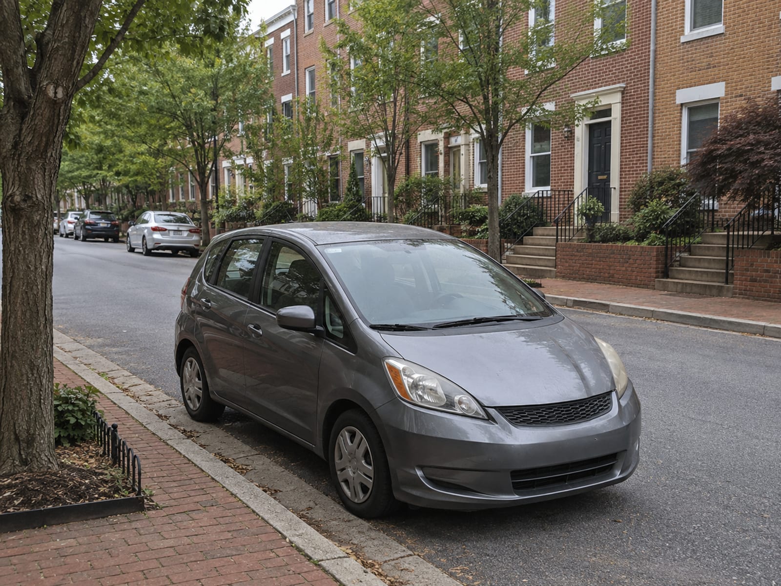 A compact car parked on a quiet suburban Maryland street lined with trees and townhouses