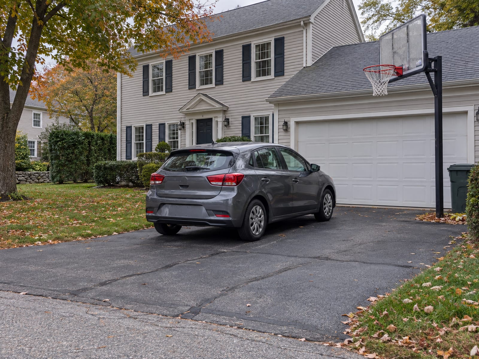 A small compact car parked in a suburban driveway beside a basketball hoop