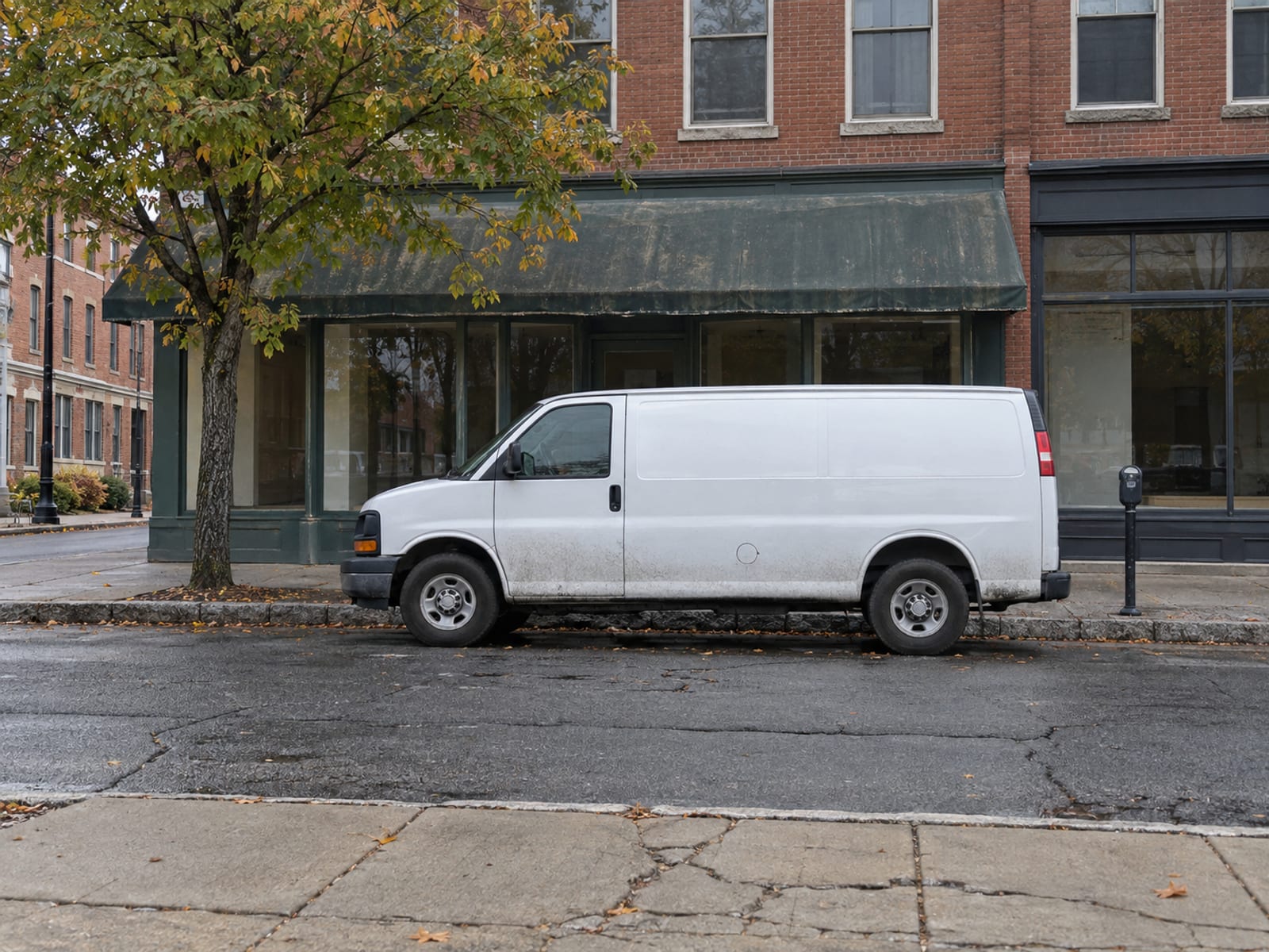 A plain white delivery van parked outside a small brick storefront with no signs