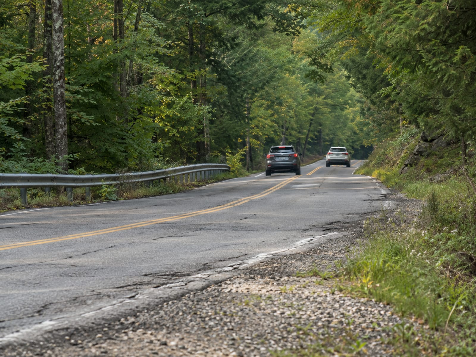 Two cars passing on a two-lane New Hampshire road through a wooded valley
