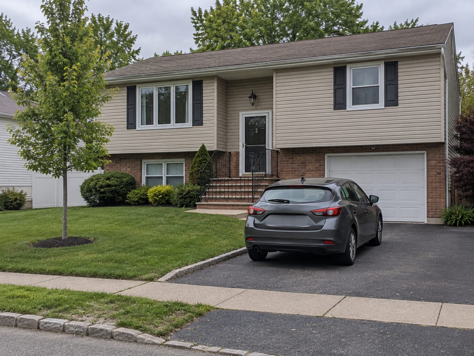 A family car parked in the driveway of a New Jersey split-level home beside a small front lawn