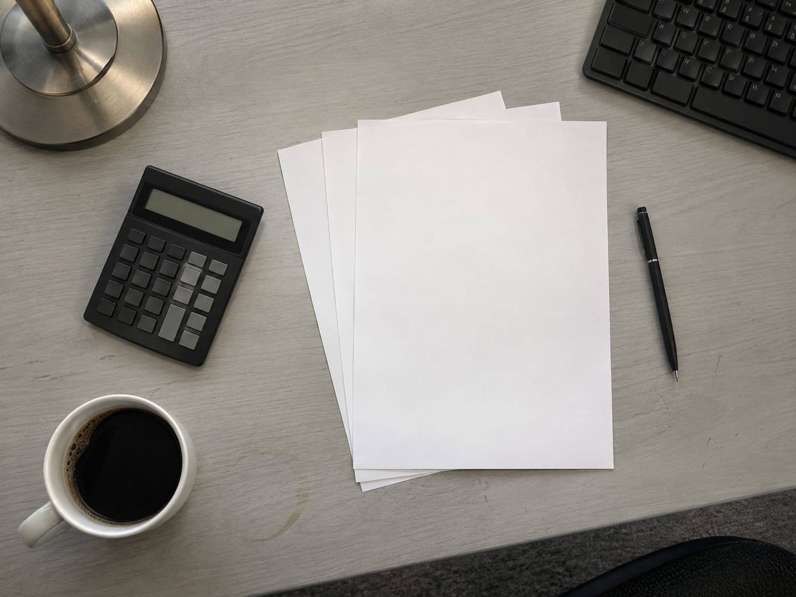 Una calculadora, un bolígrafo y hojas impresas en blanco sobre un escritorio junto a una taza de café
