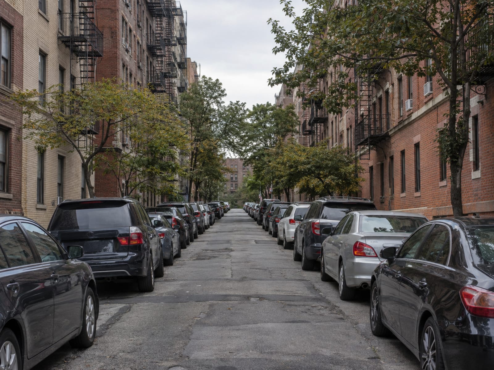 Una calle densa de la ciudad de Nueva York con casas de piedra rojiza y autos estacionados a ambos lados durante el día