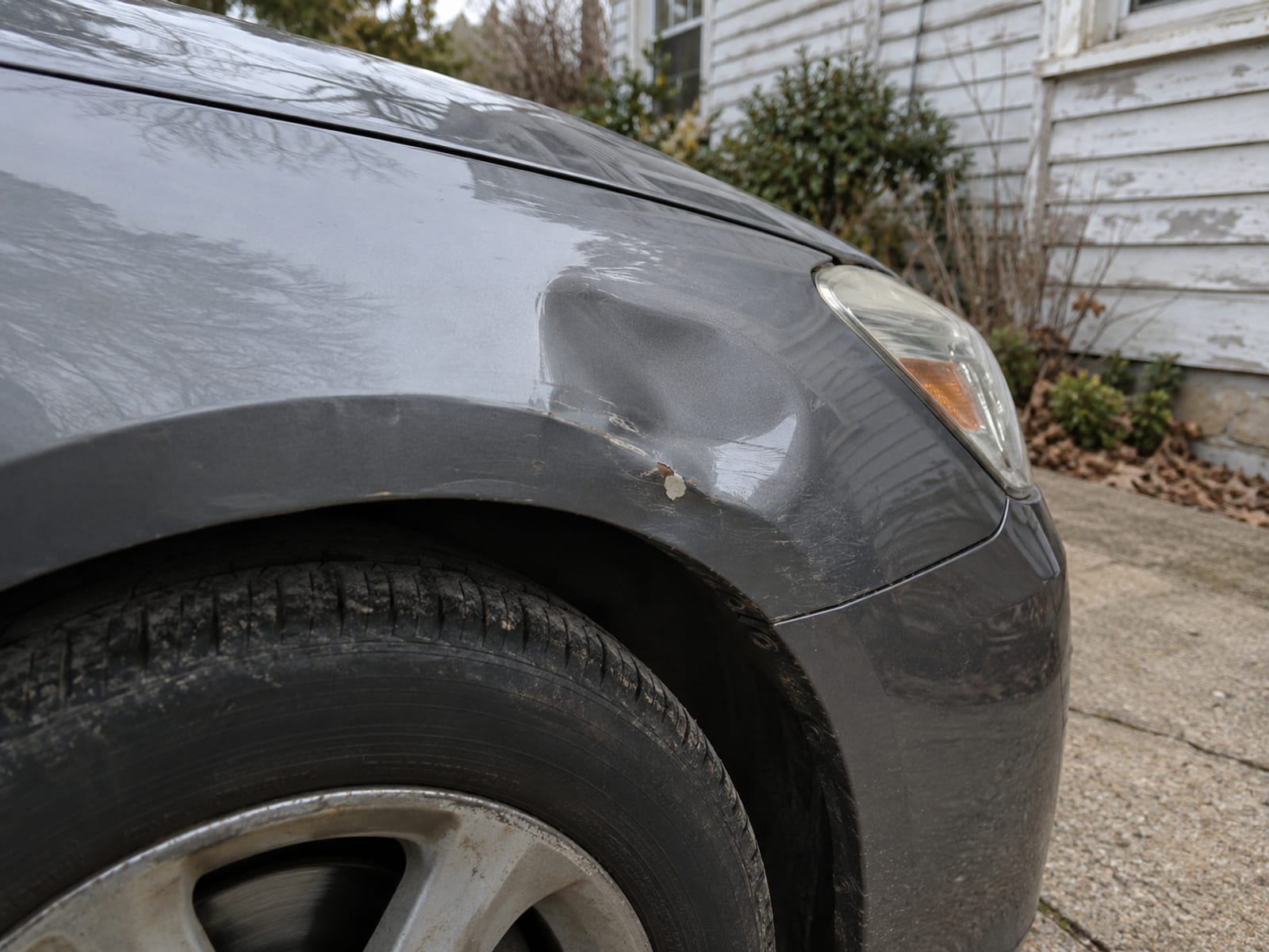 The front fender of a parked sedan with a small dent, seen in a residential driveway