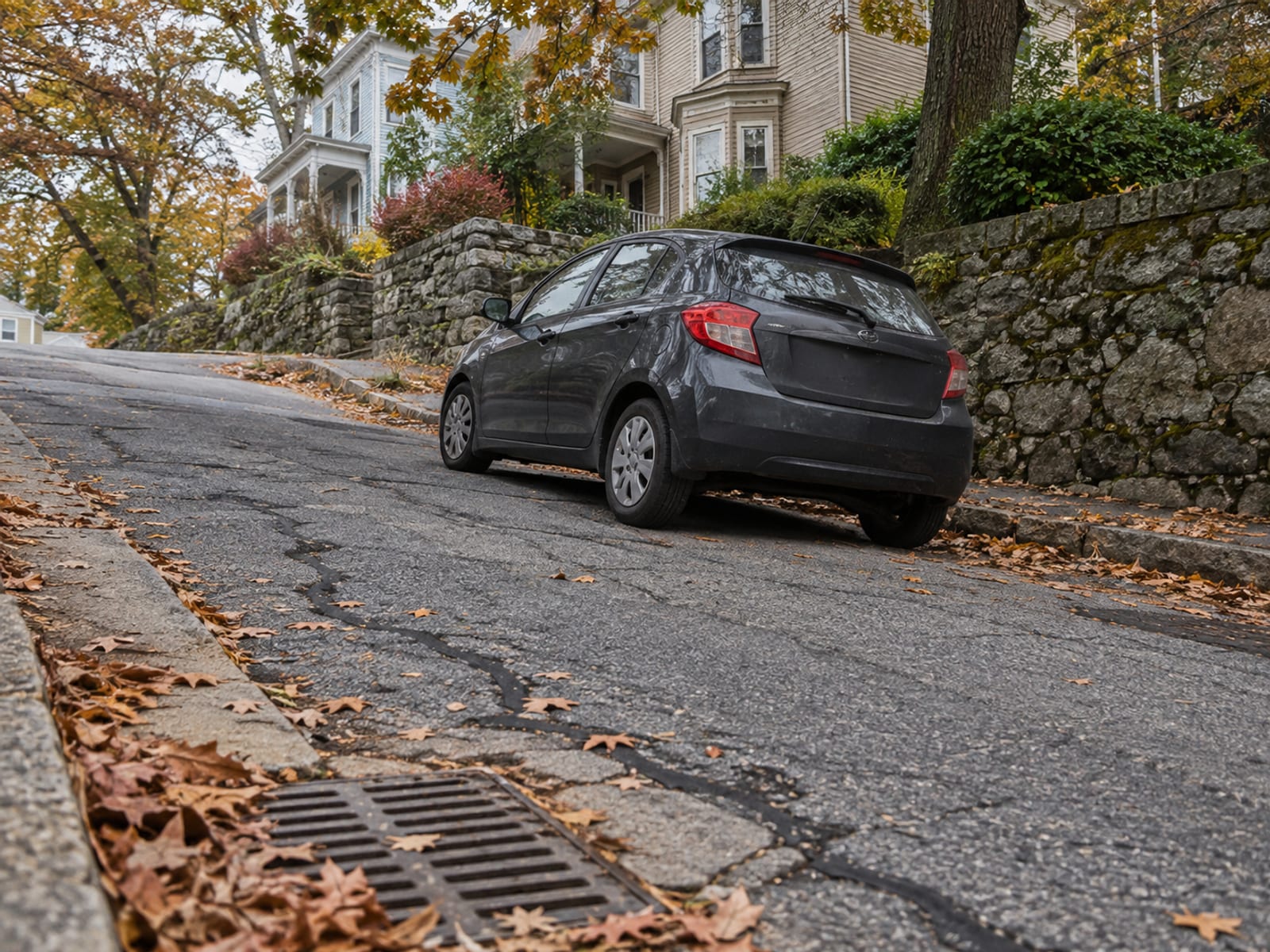 A compact car parked on a hilly city street lined with clapboard houses