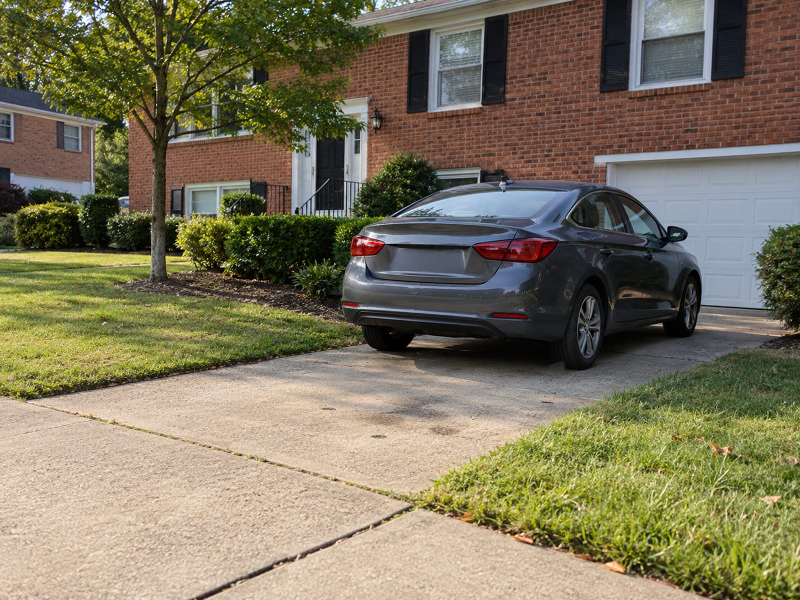 A compact car parked in the driveway of a brick Virginia house with a small front lawn