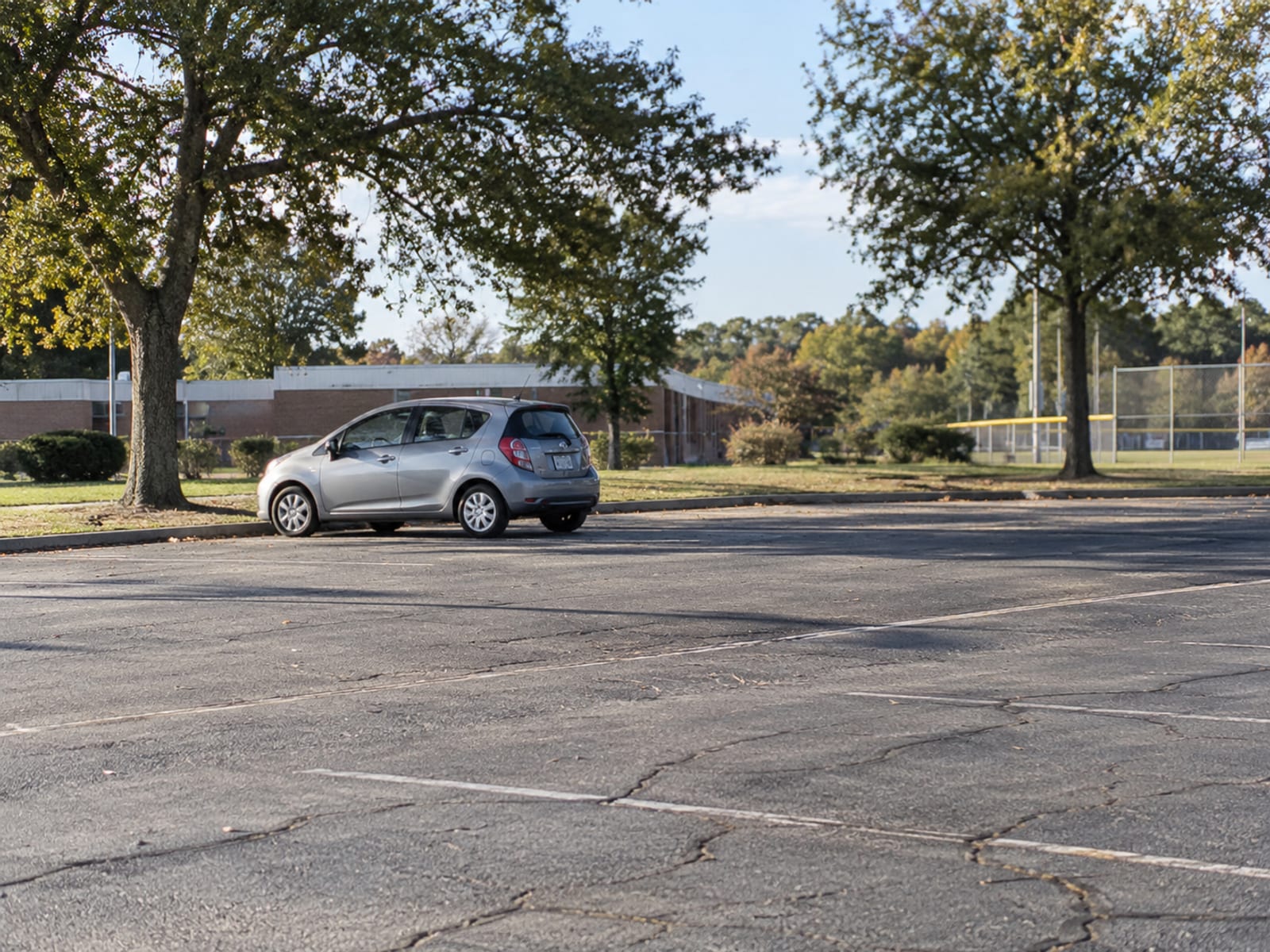 A small hatchback parked outside a suburban high school parking lot on a sunny afternoon