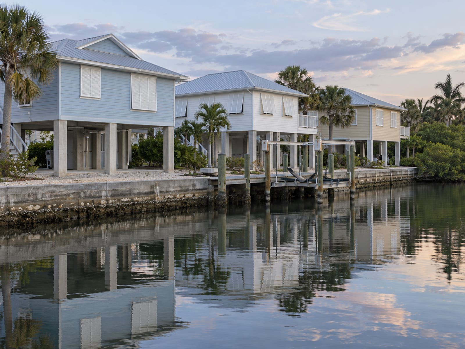 Raised coastal homes on pilings near a canal at sunset