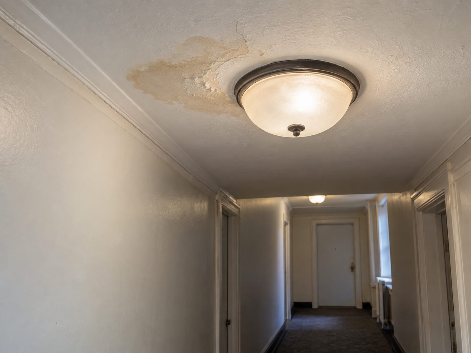 El techo de un pasillo con una pequeña mancha de agua cerca de una lámpara en un edificio de apartamentos
