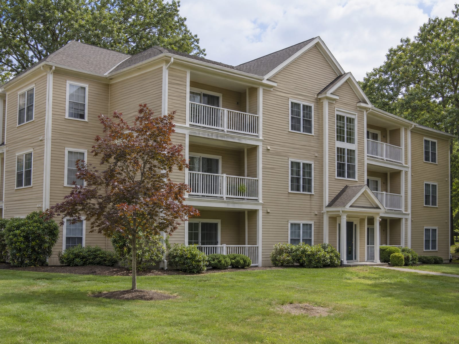 A three-story wood-sided condominium building with balconies and a small lawn in a Connecticut suburb