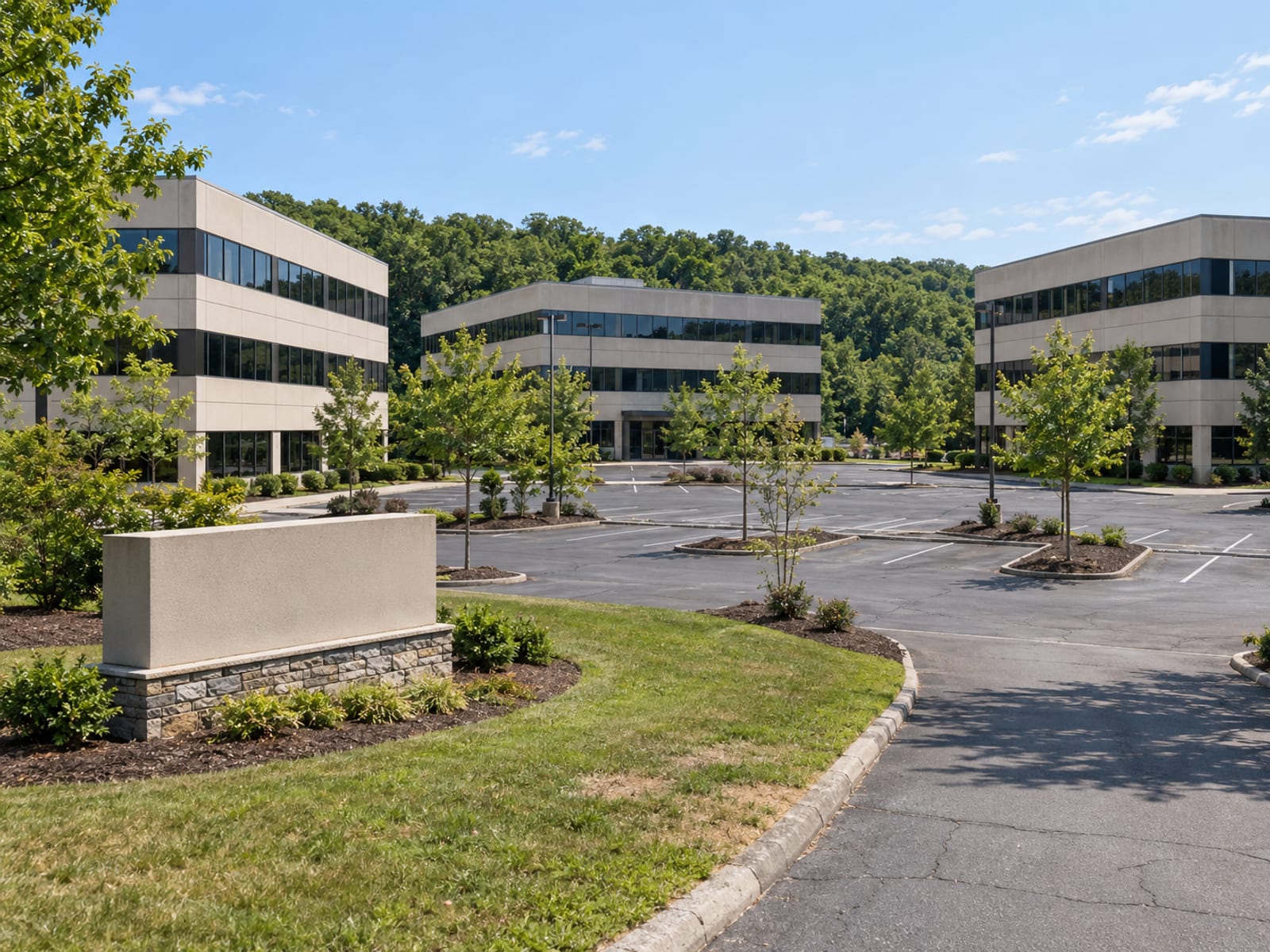 A suburban office park with several low glass buildings, a walkway lined with plantings and a parking area on a sunny day