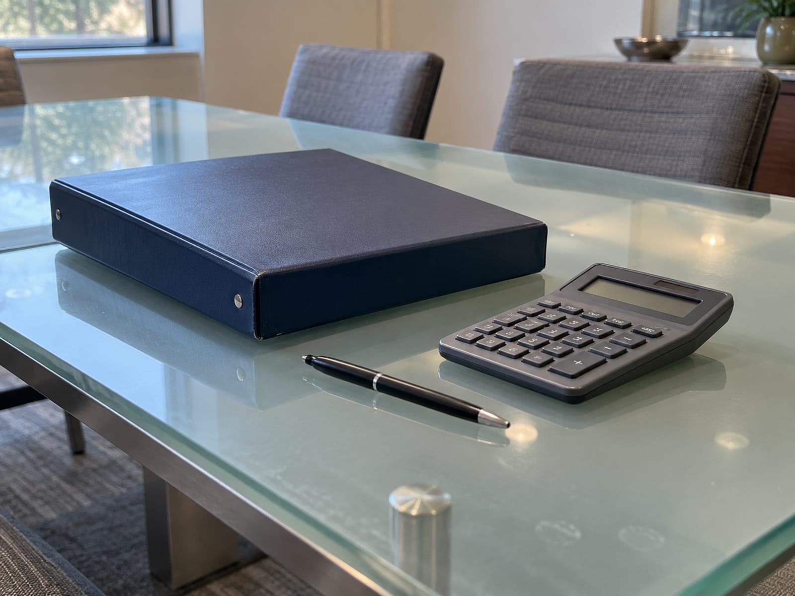 Una carpeta de préstamo cerrada, una calculadora y una pluma sobre una mesa de reuniones en una oficina tranquila