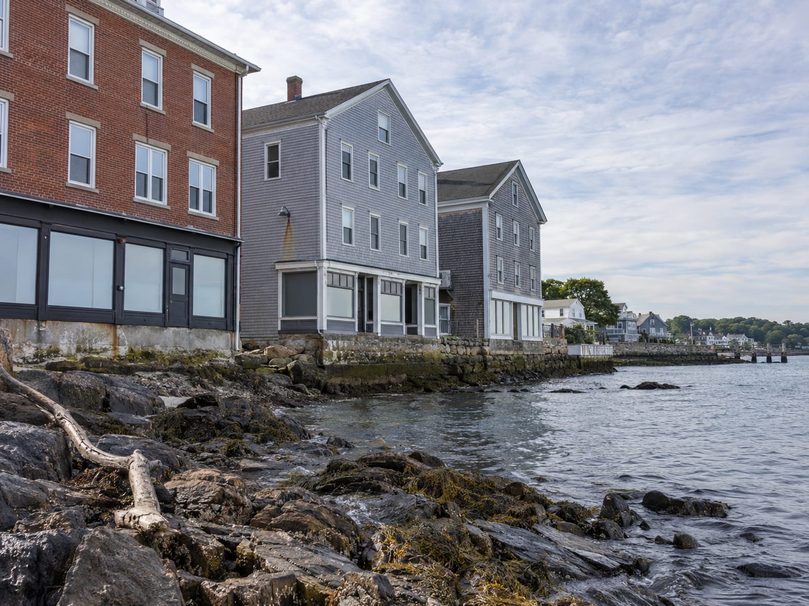 A row of mid-rise apartment buildings and a small retail strip along a harbor with boats moored in calm water