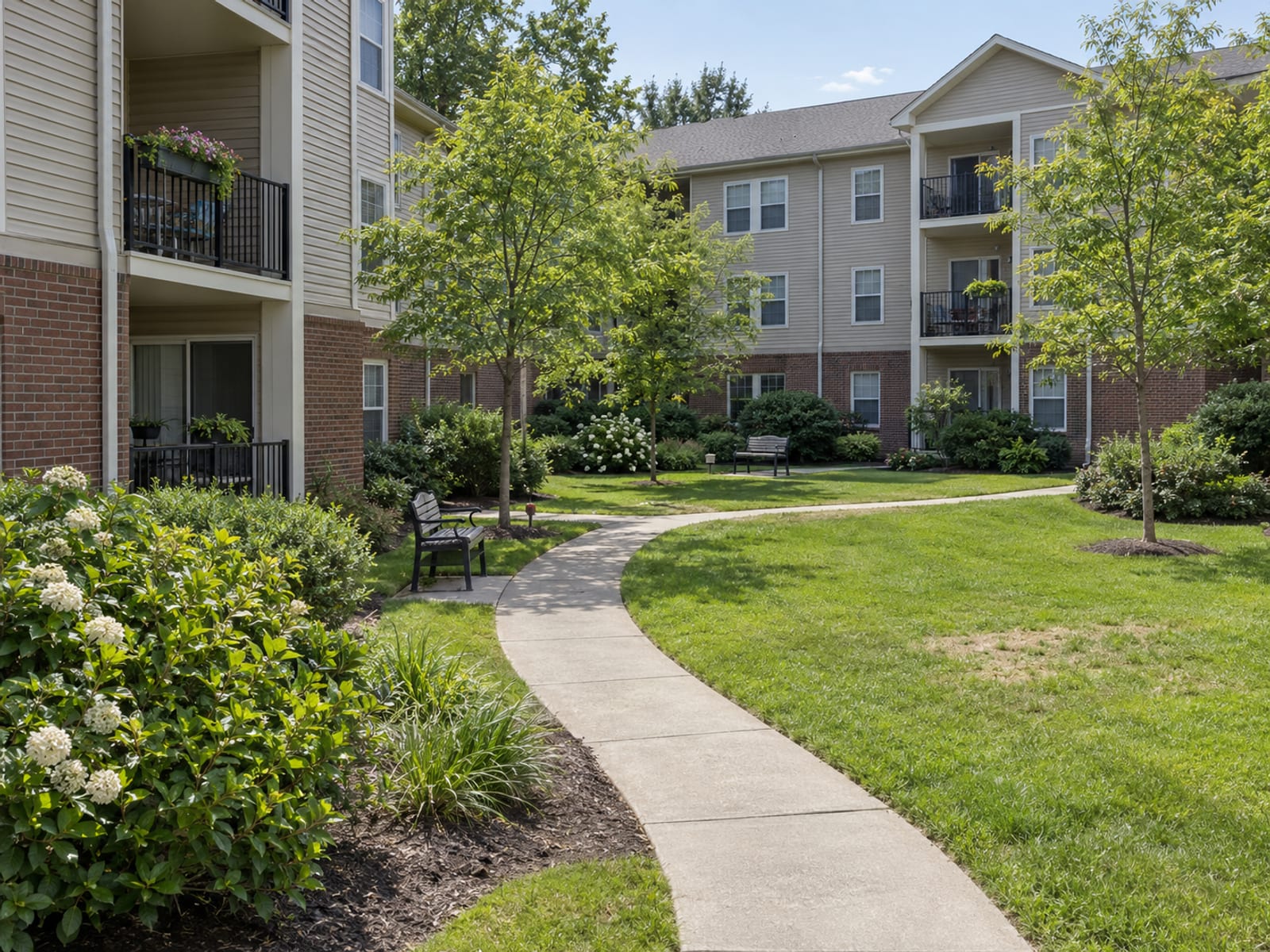 A courtyard between three-story apartment buildings with balconies and landscaped walkways on a clear day