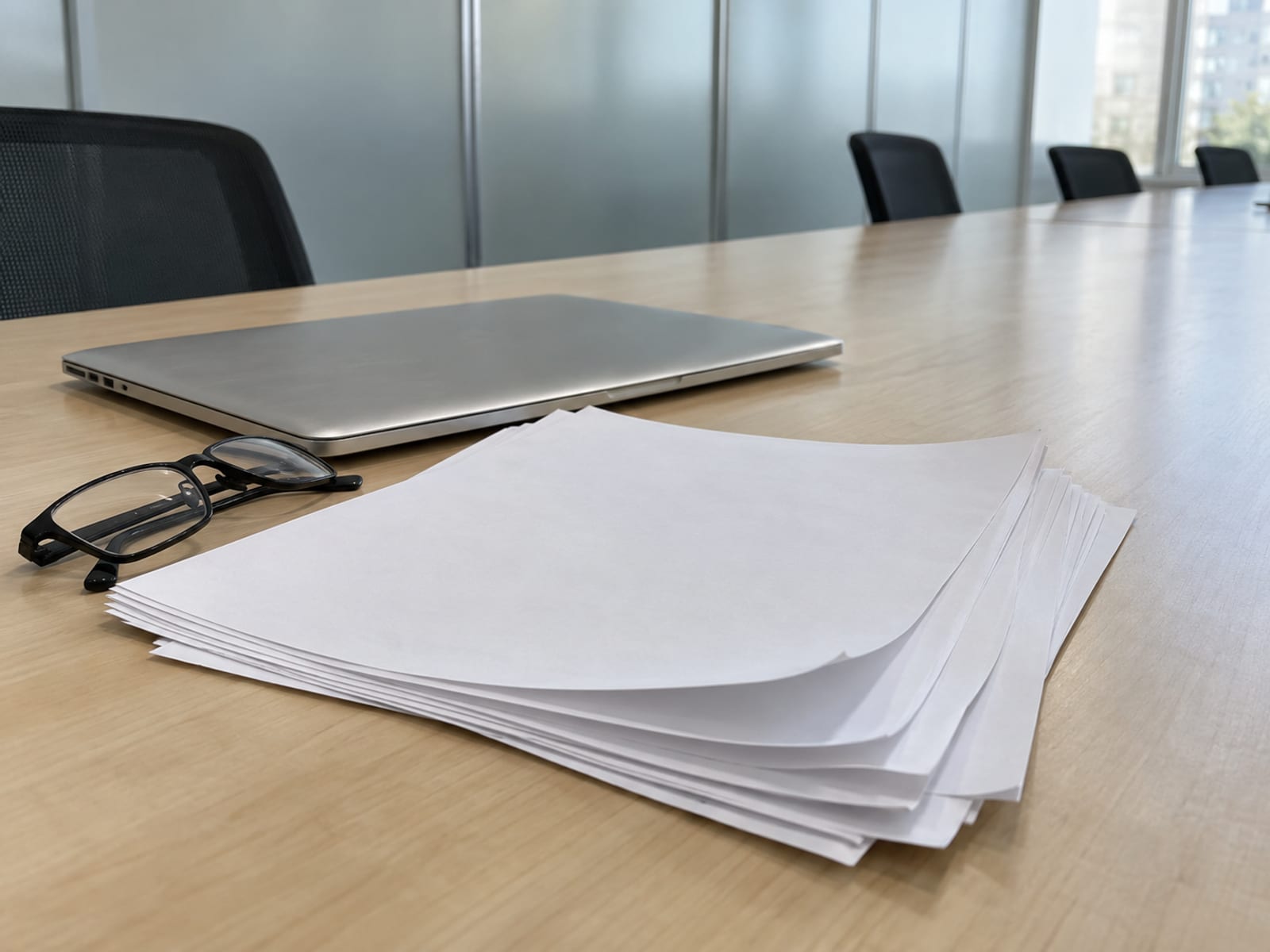 A printed lease with blank pages fanned out on a conference table beside a closed laptop and reading glasses