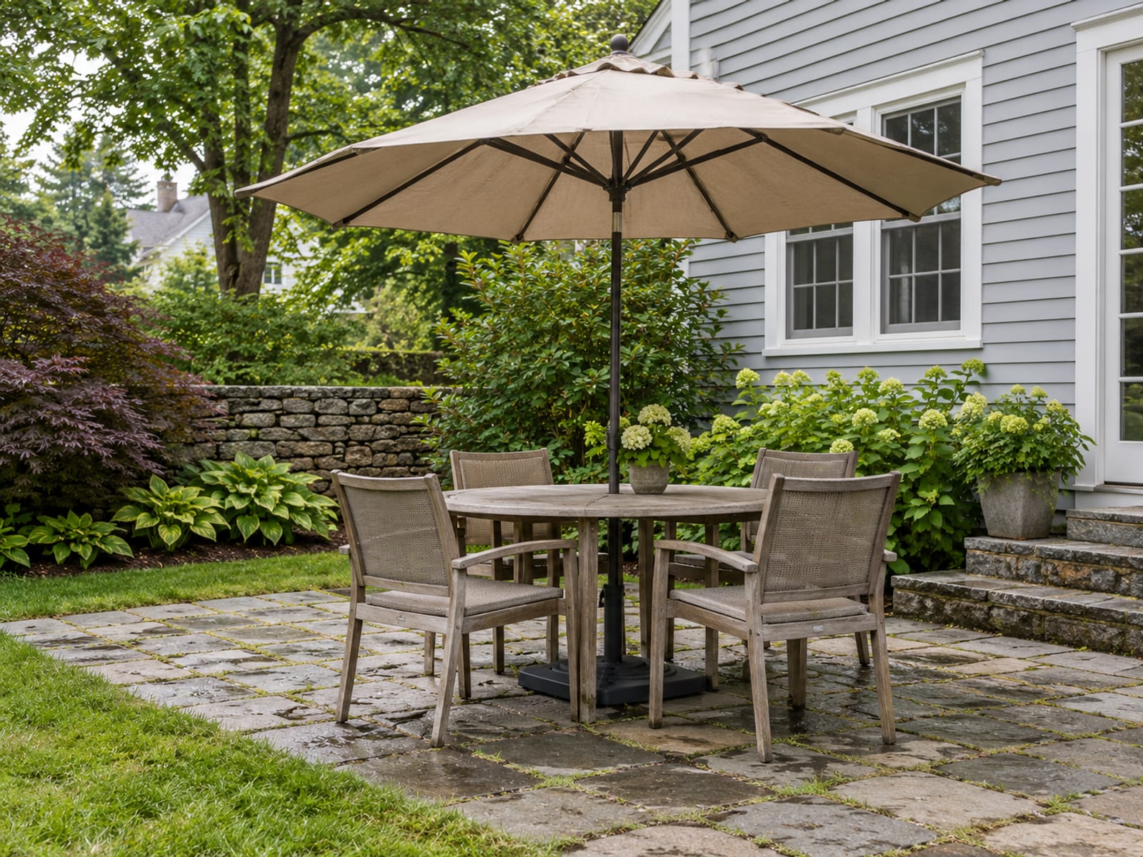 A large patio umbrella shading a backyard table beside a house on a sunny afternoon