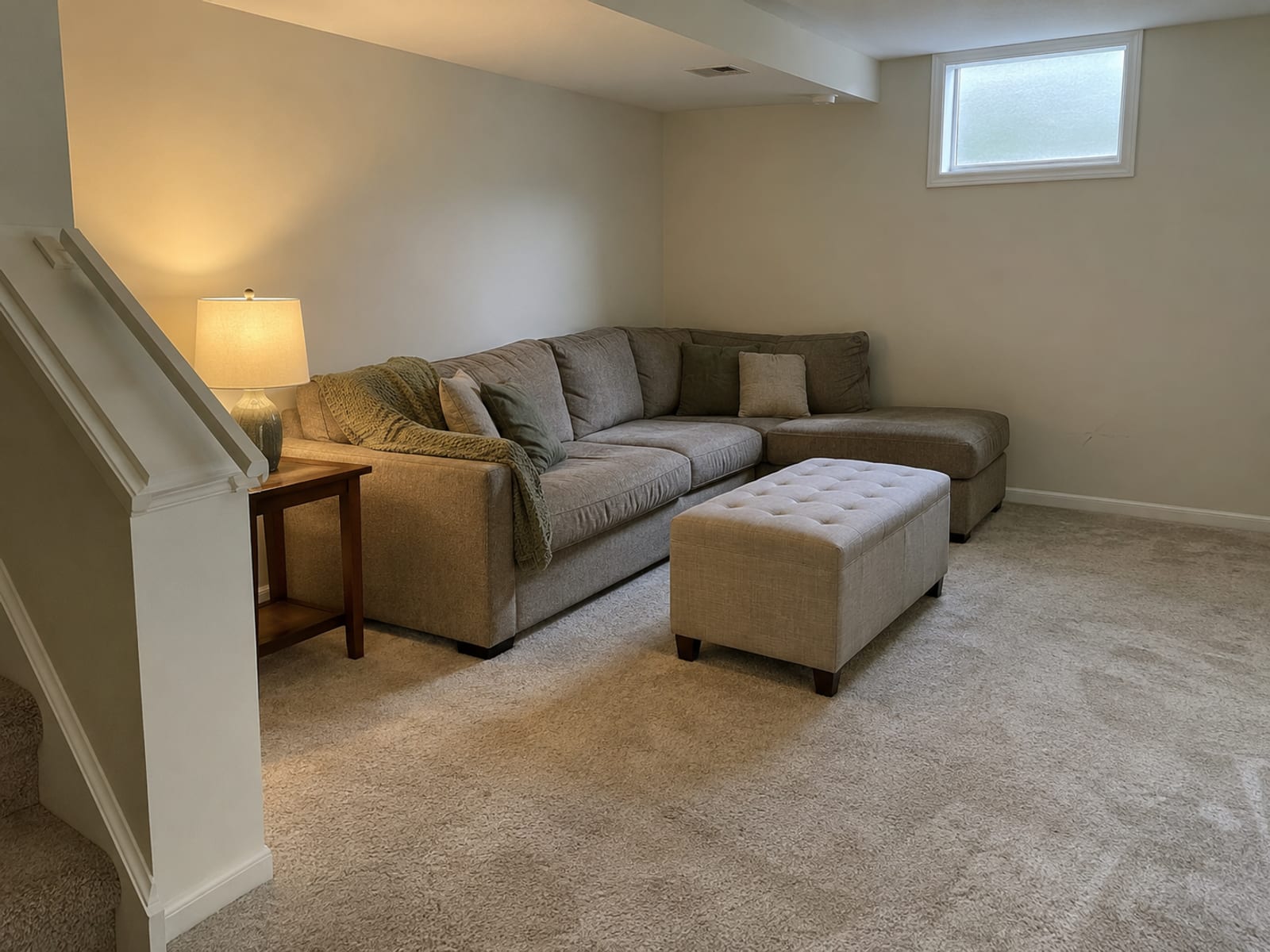 A finished basement room with carpet, a sofa and a small window near the ceiling
