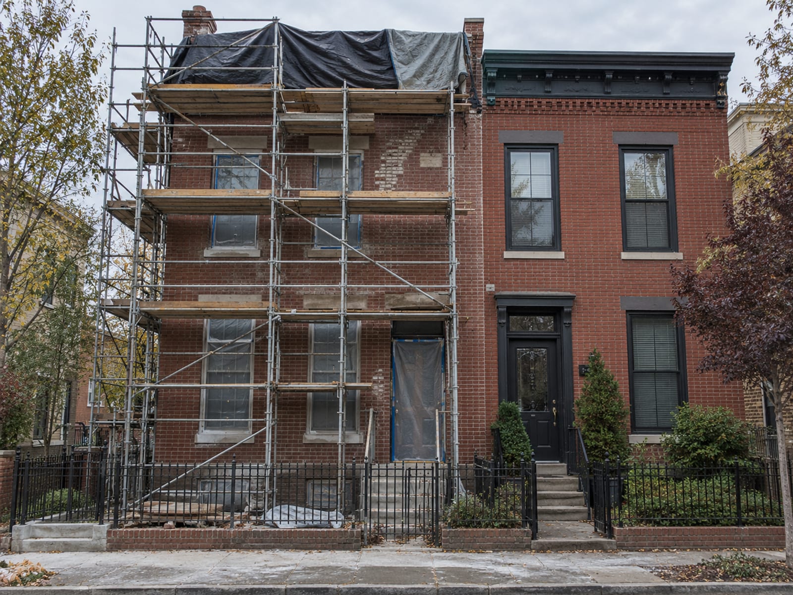 Two attached brick rowhouses sharing a party wall, one with scaffolding along its facade