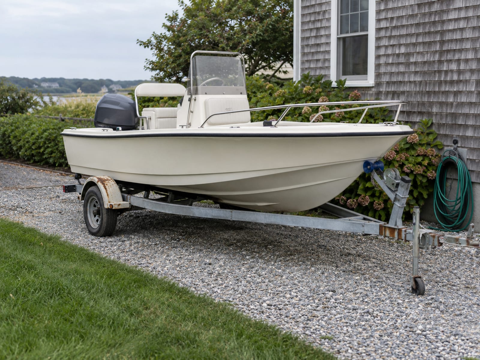 A small powerboat on a trailer parked in a driveway beside a shingled coastal house
