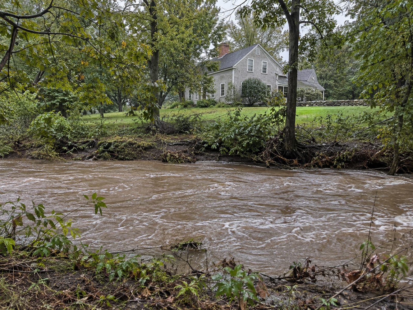 A wooden house beside a tree-lined creek running high after heavy rain
