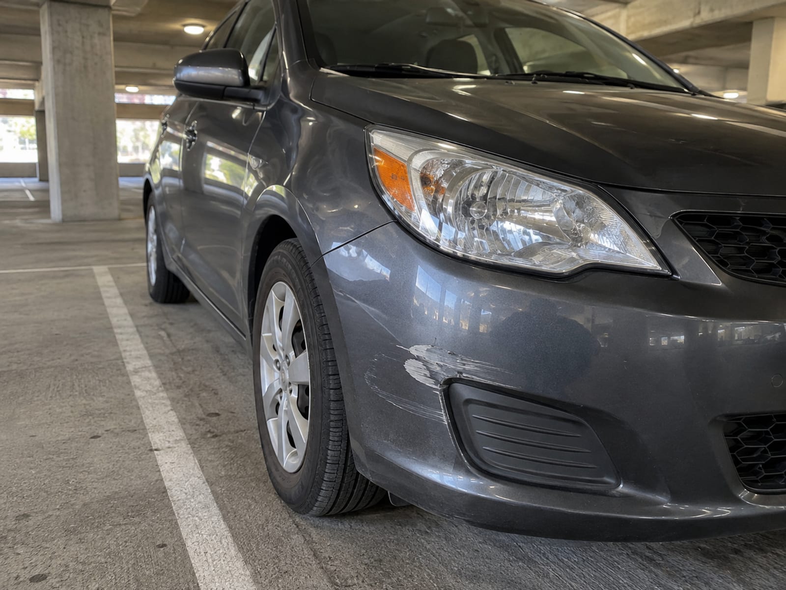 Un auto compacto con la defensa delantera raspada estacionado en un estacionamiento techado y vacío