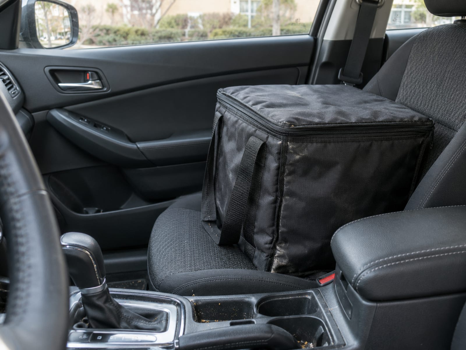 A plain insulated delivery bag on the passenger seat of a parked car