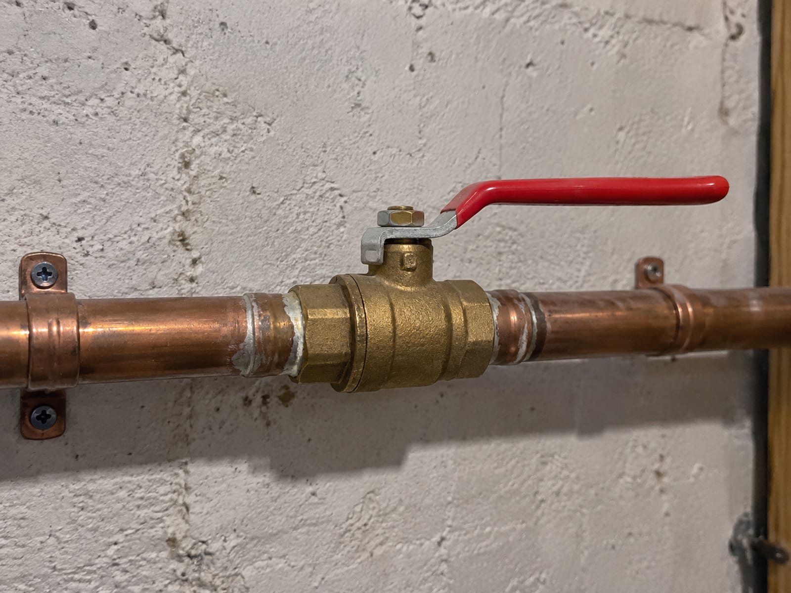 A water shut-off valve on a copper pipe along a basement wall