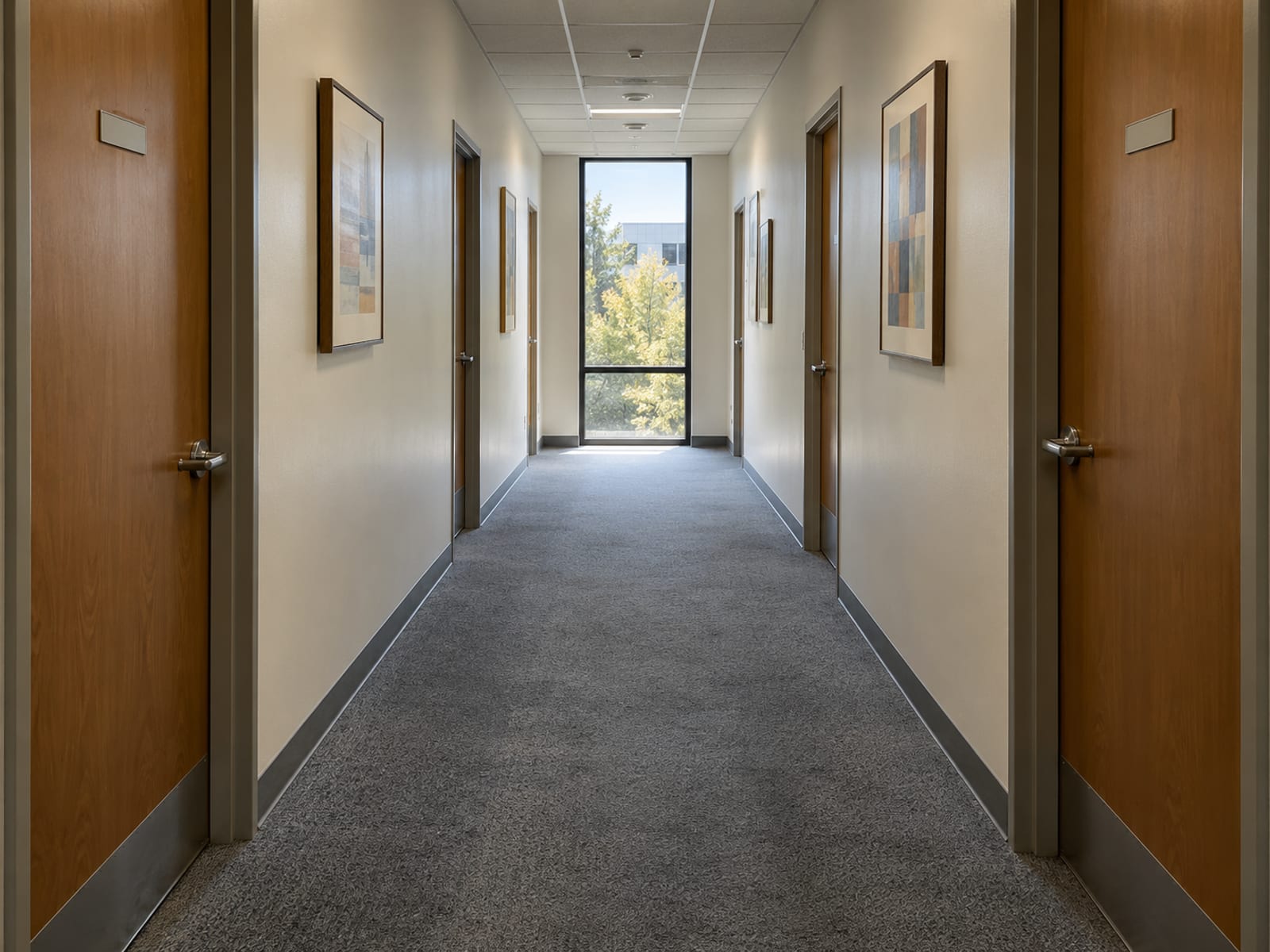 A quiet office hallway with closed doors and a window at the far end