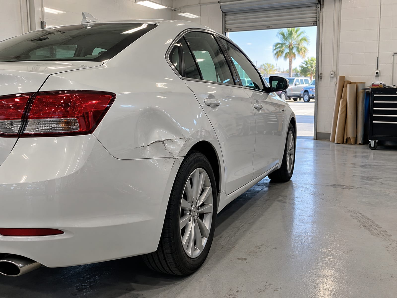 A sedan with a dented rear quarter panel parked in a clean repair shop bay