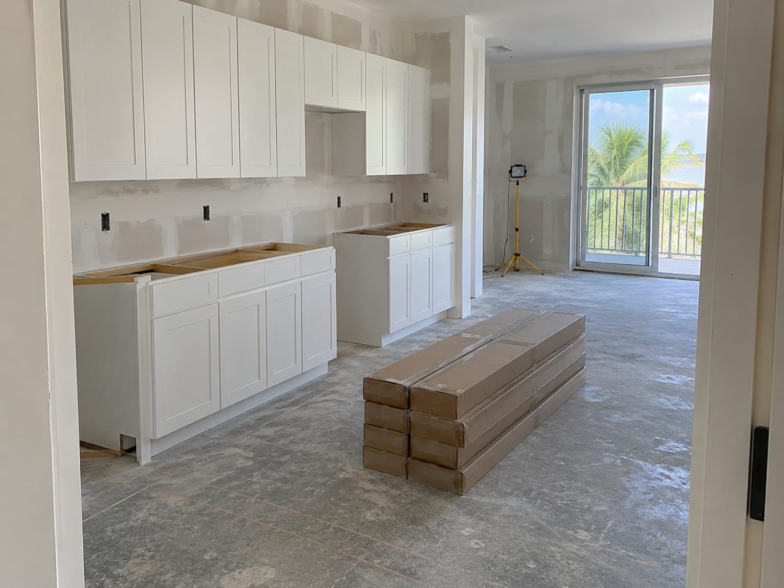 An unfinished condo kitchen with bare drywall, new cabinets and flooring materials stacked on the floor