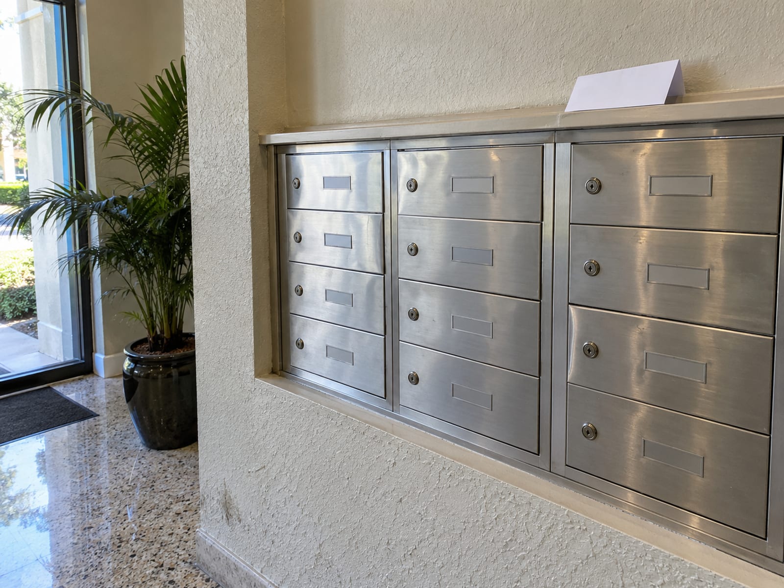 A row of closed mailboxes in a condominium lobby with a folded notice resting on top