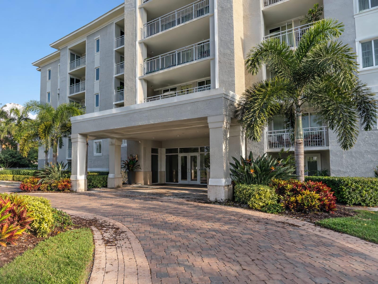 A mid-rise condominium building with balconies and a covered entry under a clear sky