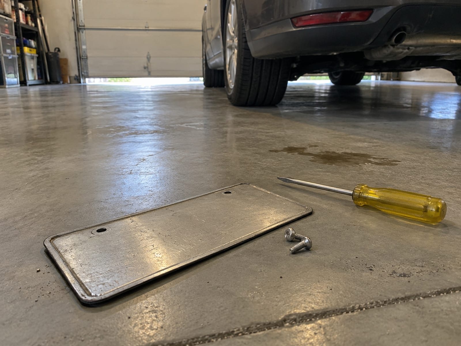 A license plate lying face down beside a screwdriver on a garage floor