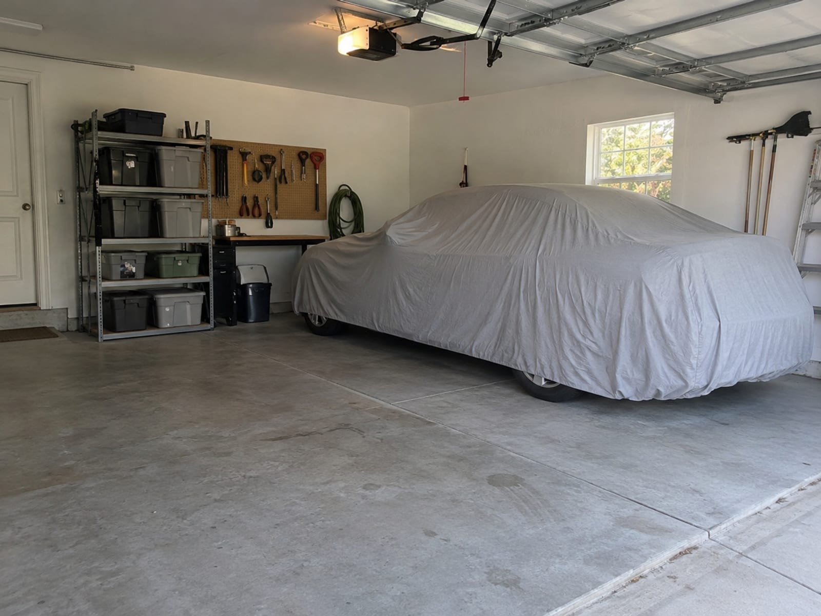 A car under a fitted cloth cover in a tidy home garage