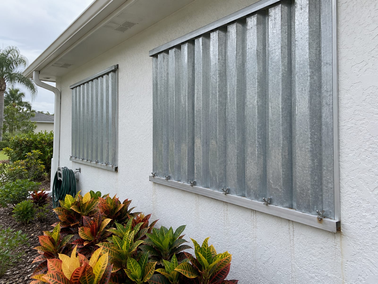 Metal hurricane shutters closed over the windows of a stucco house