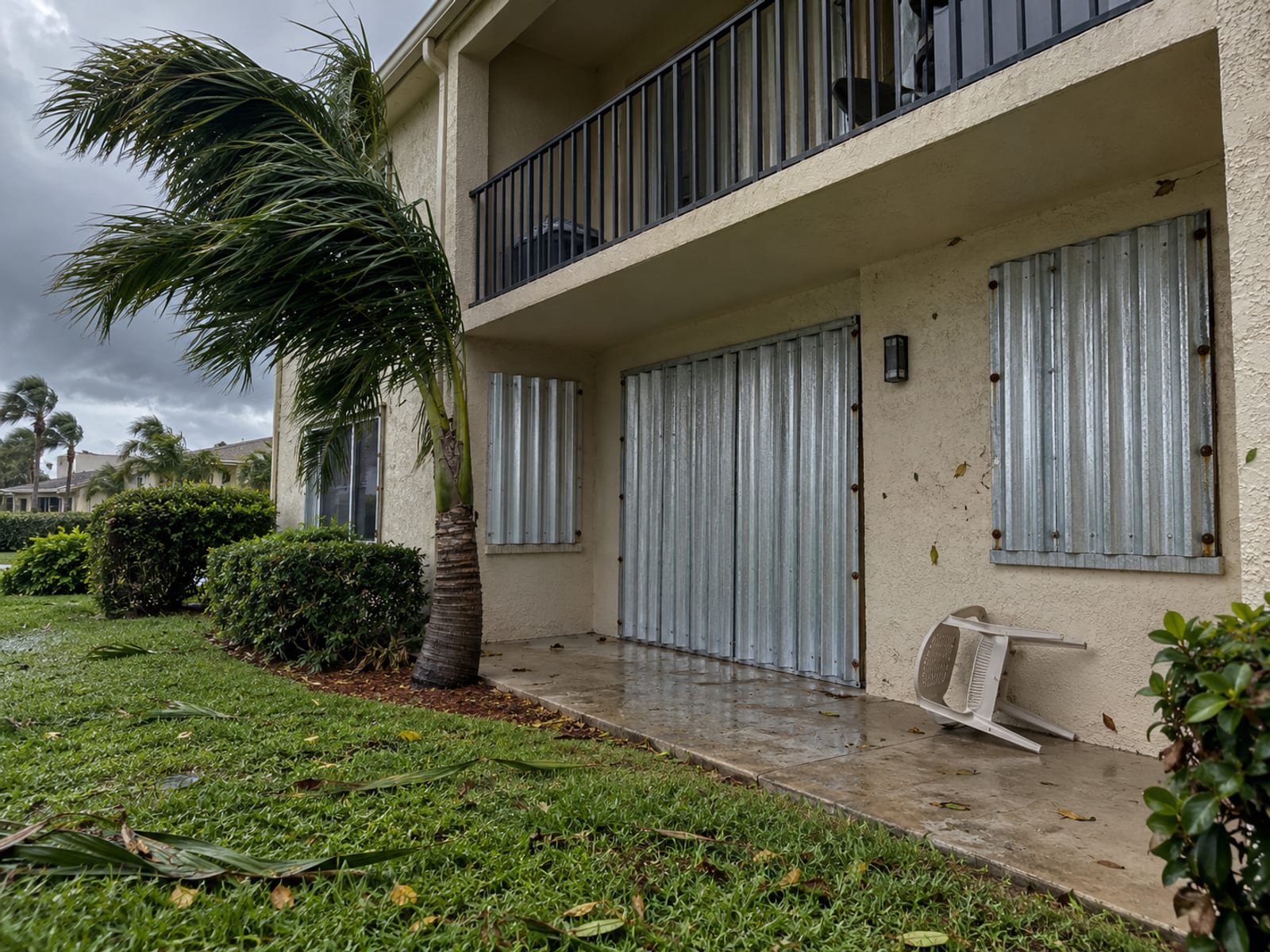 Storm shutters closed over the windows of a ground-floor apartment under a gray sky