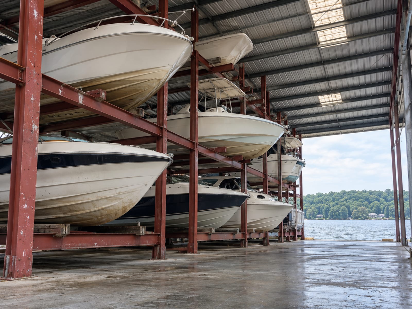 Several powerboats resting on racks in a covered dry-storage building at a lake